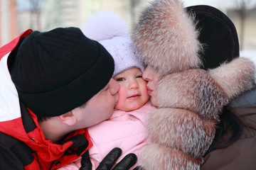 mother and father kissing his little daughter, winter