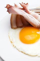bacon with  fried  eggs on a plate, fork and bread isolated on w