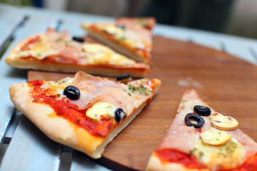 Sliced pizza with ham and olives on a wooden board
