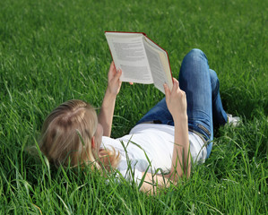 Junge Frau liest ein Buch auf einer Wiese