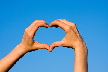 Hands forming heart against blue sky