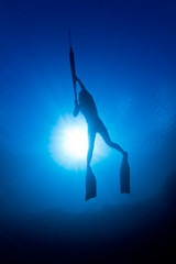 A girl spearfishing infront of the sun