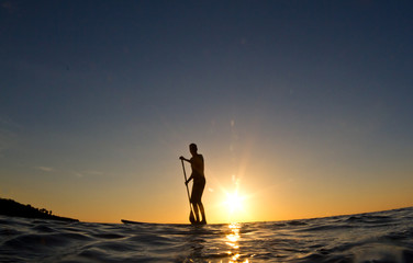 Silhouette of a man paddling his surf board at sunset