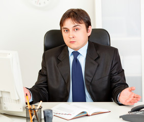 Confused modern businessman sitting at office desk.