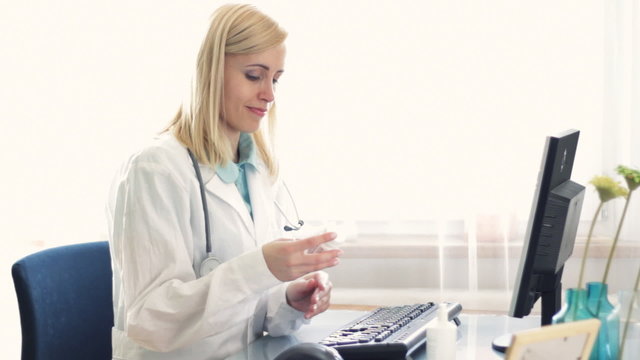 Female doctor working on computer and checking pills bottle