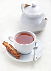 Cup of tea with cookie near the teapot  on white table