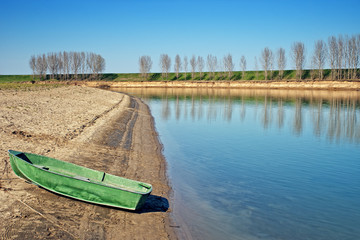 Green boat on sunlit sand river bank with blue sky