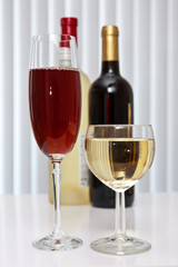 wineglasses of red and white wine with two bottles