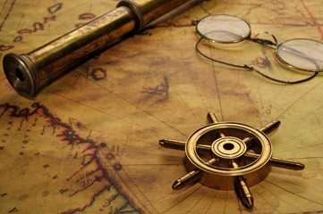 Steering wheel, glasses and spyglass on the old map