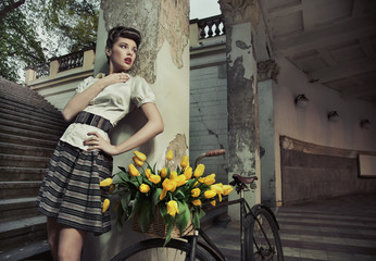 Piękna brunetka pozuje przy rowerze z żółtymi tulipanami - obrazy, fototapety, plakaty