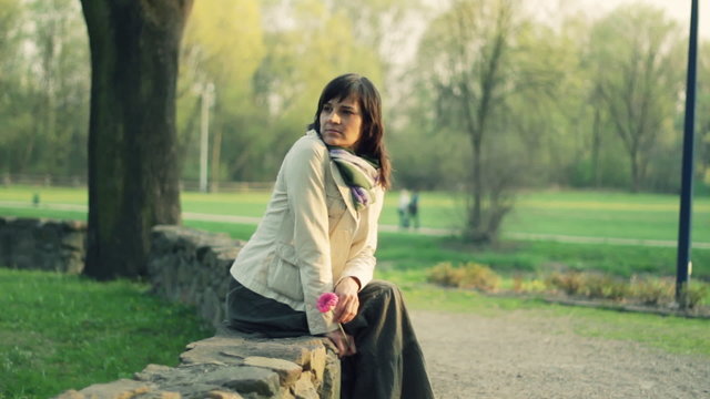 Pensive woman with flower in the park, dolly shot