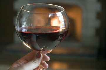 A glass of red wine by a lit fireplace.