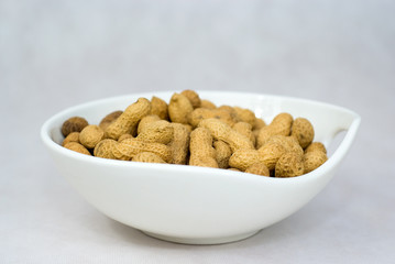 Pile of ripe crude peanuts in white bowl