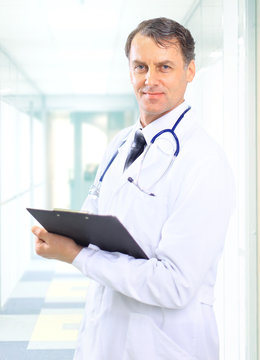 Happy smiling mature doctor writing on clipboard in a