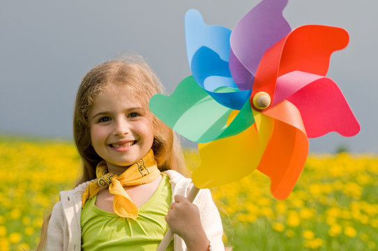 Girl with colorful pinwheel on dandelion meadow
