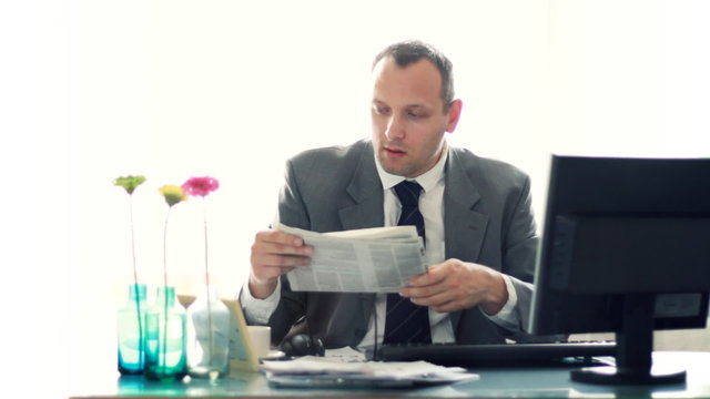 businessman working on computer and looking into newspaper