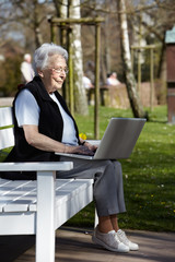 Nette alte Dame mit Laptop auf Bank 35