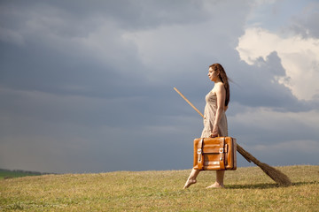 Young witch at grass field with broom in storm day.