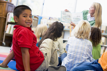 Kindergarten teacher reading to children in library, boy looking