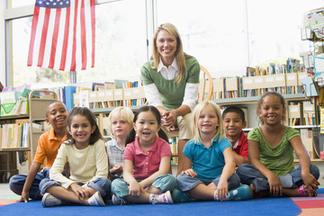 Kindergarten teacher sitting with children in library - Powered by Adobe