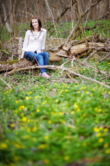 Beautiful young woman sitting on a branch in a spring park