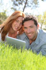 Portrat of couple laying down the grass with touchpad