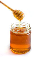 Honey dripping into jar over white