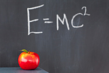 Stack of books with a red apple and a blackboard with a formula
