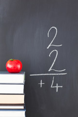 Stack of books with a red apple and a blackboard with a simple f © WavebreakMediaMicro