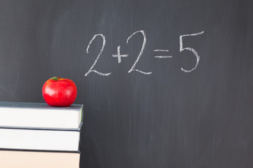 Stack of books with a red apple and a  blackboard with 