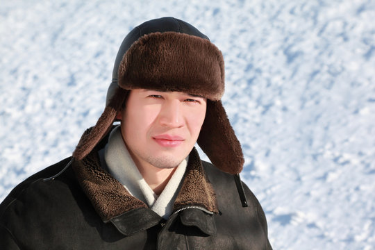 Young man stands in ear-flaps hat in winter