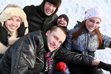 Young people by winter day lie on snow in heap and laugh