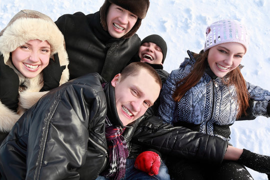 Young people by winter day lie on snow in heap and laugh