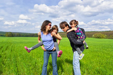 Happy family outdoors. Parents giving their kids piggyback ride