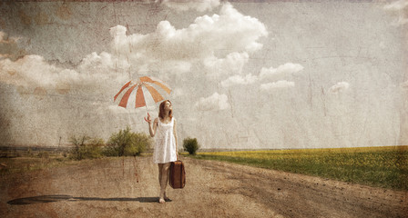 Lonely girl with suitcase and umbrella at country road.