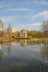 Беседка на острове, посереди пруда, отражающаяся в воде.