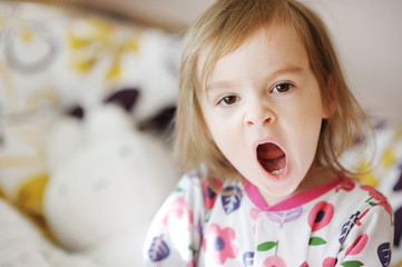 Little yawning toddler girl in pajamas on sunny morning