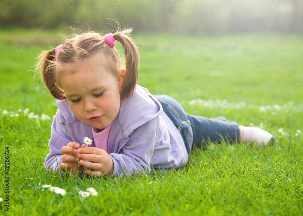 Wall mural little girl is laying on green meadow