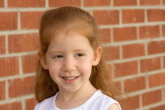 Portrait Of Young Redhead Kid Girl By Brick Wall