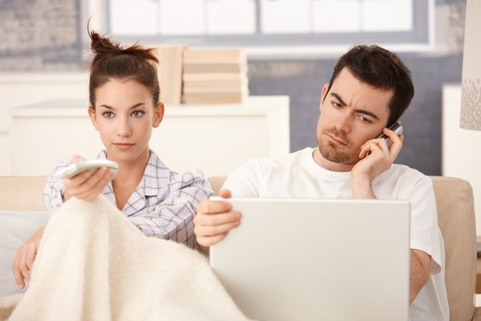 Young couple in bed man working woman watching tv