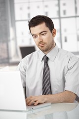Fototapeta premium Young man working on laptop in bright office