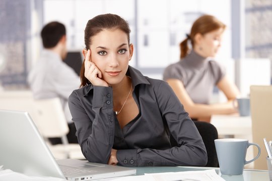 Young woman sitting at desk others working behind