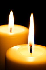 Two Lit Orange candles on black background, selective focus