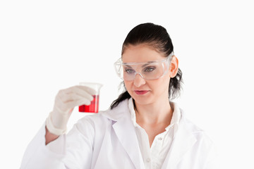 Dark-haired scientist looking at a red beaker