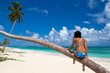 Tanned woman sitting on a palm white sand beach