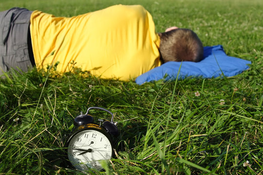 man in yellow shirt sleeping on summer lawn near alarm clock, ha
