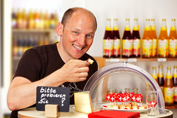 man tasting Swiss cheese in a wholefood shop