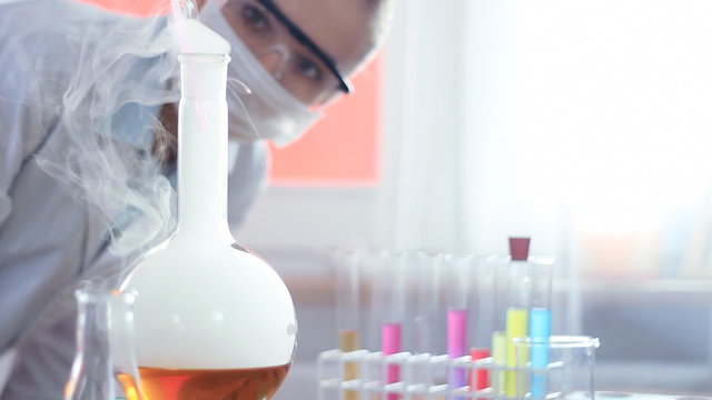 Female scientist examinines smoky Volumetric Flask