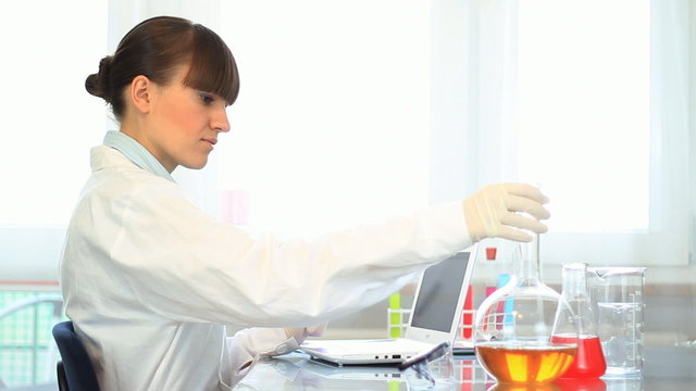 scientist working on laptop and examining volumetric flask