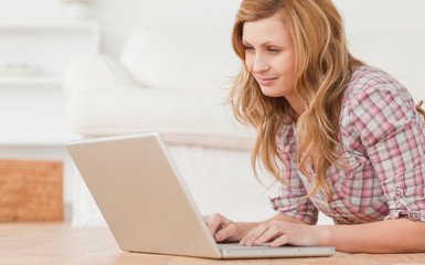 Blond-haired woman working on her laptop lying down on the floor